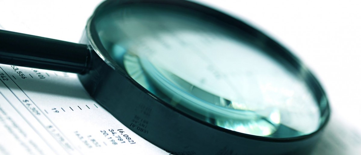 12420575 - magnifying glass over financial figures.  soft focus, cyan tone.