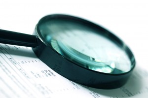 12420575 - magnifying glass over financial figures.  soft focus, cyan tone.