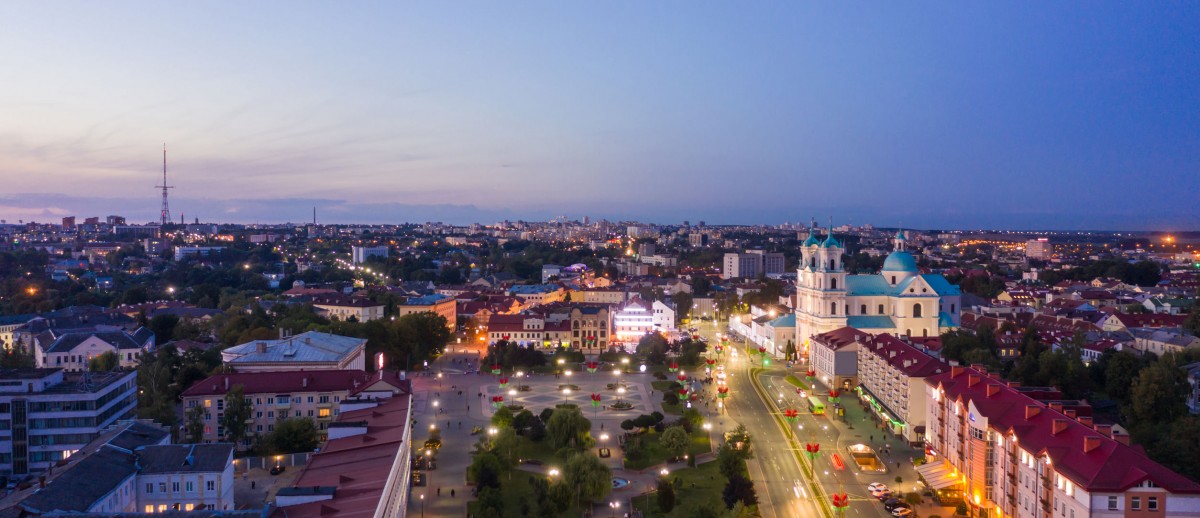 St. Francis Xavier Cathedral And Traffic In Mostowaja And Kirova Streets At Evening In Night Illuminations Lights. Sunset Sky. Grodno city in Belarus