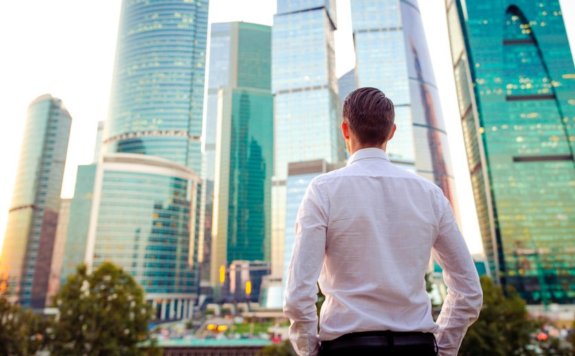 Back view of businessman looking on copy space while standing against glass skyscraper