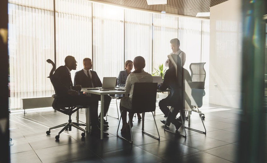 Silhouettes of people sitting at the table. A team of young businessmen working and communicating together in an office. Corporate businessteam and manager in a meeting